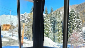 Um sofá azul num quarto com grandes janelas com vista para uma paisagem nevada, com árvores e montanhas.