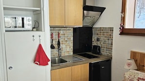 Cozinha compacta com micro-ondas, pia e lava-louças pretas.