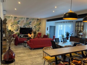 Ein modernes Wohnzimmer mit einem roten Sofa, einem Essbereich mit einem Tisch und einem Fernseher im Hintergrund.