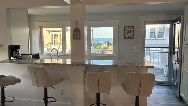 A kitchen with a large island, bar stools, and a view of the ocean. - Private Rye Beach getaway with 3 bedrooms across two units, ideal for couples or families. Enjoy private beach access, ocean views, fast Wi-Fi, and walk to Petey’s Famous Seafood—steps from the sand and coastal dining. (Rye)