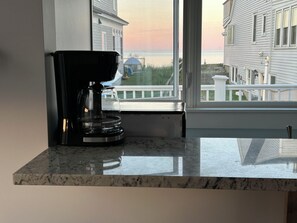 Eine Küche mit Kaffeemaschine auf einer Marmorarbeitsplatte, ein Fenster mit Blick auf ein Haus und einen Steg.