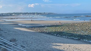 A beach with a rocky shoreline, waves, and a distant town. - Private Rye Beach getaway with 3 bedrooms across two units, ideal for couples or families. Enjoy private beach access, ocean views, fast Wi-Fi, and walk to Petey’s Famous Seafood—steps from the sand and coastal dining. (Rye)