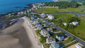 An aerial view of a coastal town with houses along the beach, a road, and a river. - Private Rye Beach getaway with 3 bedrooms across two units, ideal for couples or families. Enjoy private beach access, ocean views, fast Wi-Fi, and walk to Petey’s Famous Seafood—steps from the sand and coastal dining. (Rye)