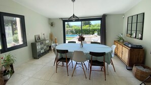 A dining area with a table set for six, a wooden cabinet, and a large window with a view of greenery. - House with swimming pool and large garden near the sea (Montbazin)