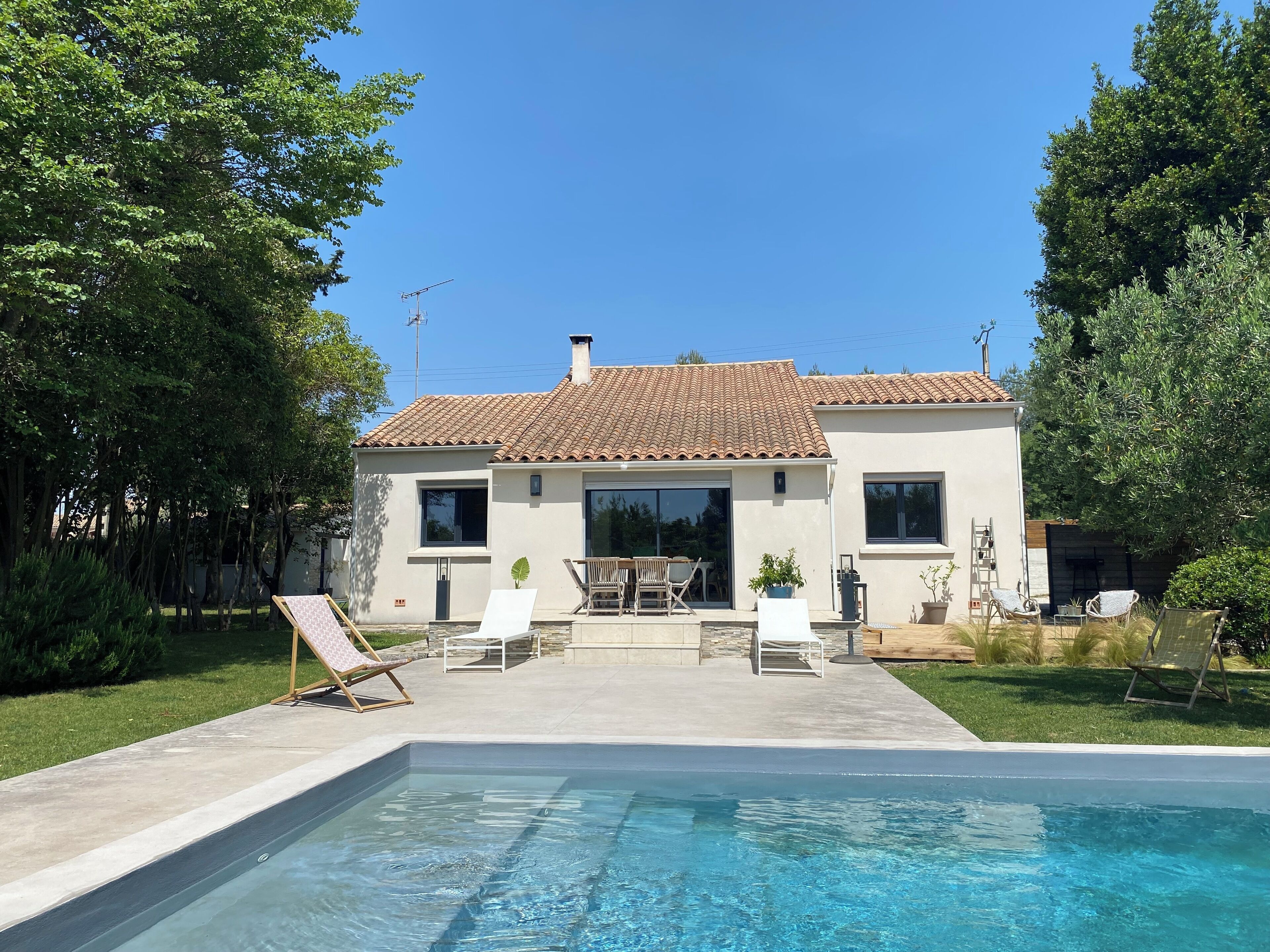 A two-story house with a swimming pool, surrounded by trees and a well-maintained lawn.