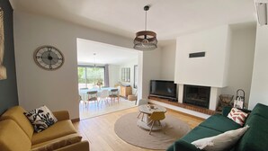 A spacious living room with a sofa, a coffee table, and a television. There is a fireplace and a large window. - House with swimming pool and large garden near the sea (Montbazin)
