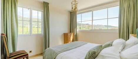 Une chambre à coucher comprenant un lit, une chaise, une commode et une fenêtre donnant sur le paysage.
