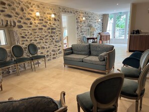 A room with a stone wall, a sofa, and several chairs. - Mas de Louise (LUSSAS)