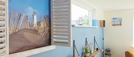 A room with a blue wall, a window with shutters, a shelf with decorative items, and a chair.