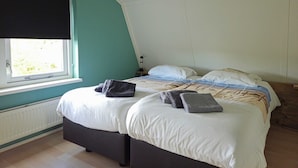 Et soveværelse med to senge, et vindue med rullegardin, en radiator og et natbord med lampe.