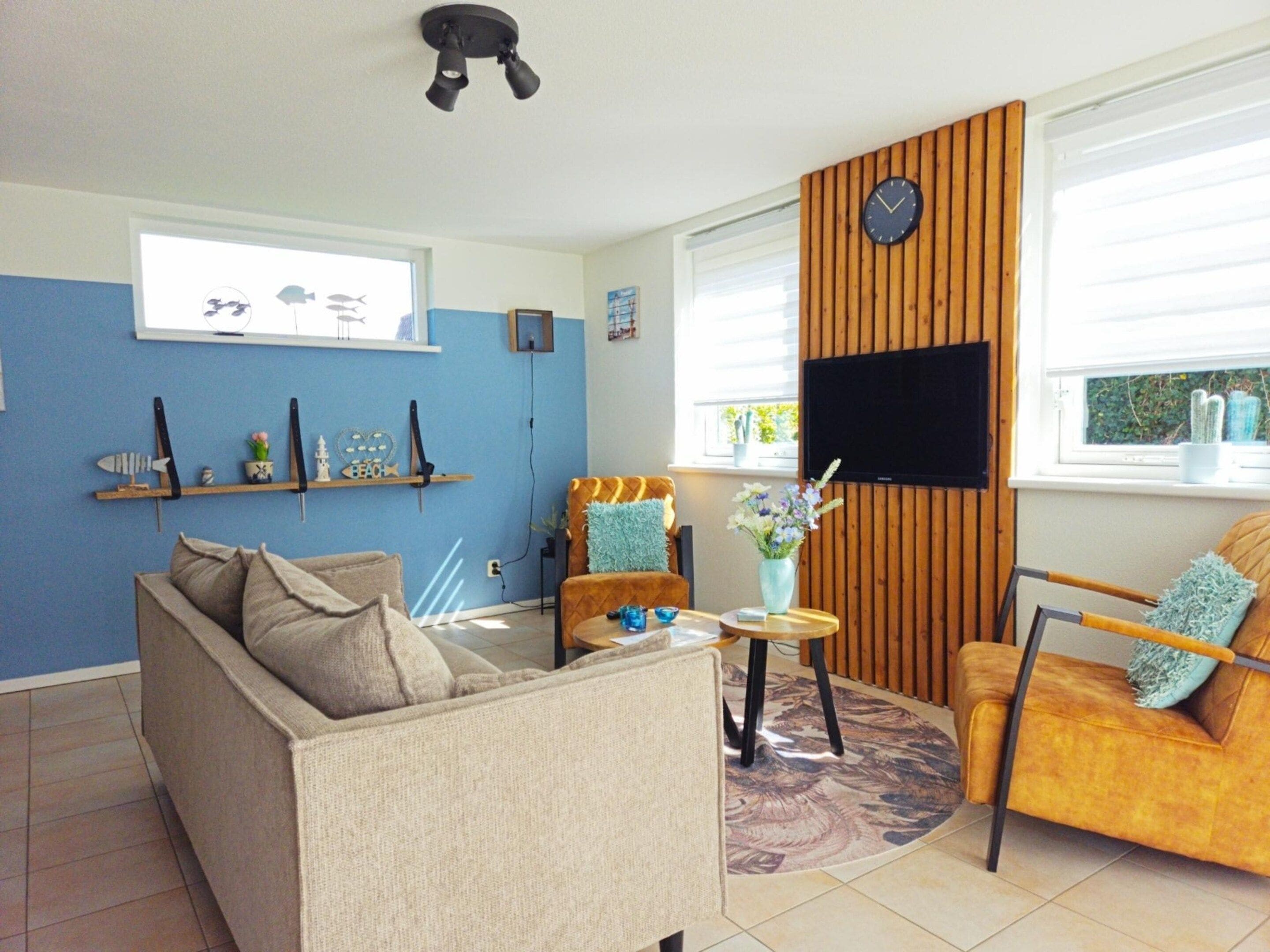 A living room with a sofa, armchair, coffee table, and a TV mounted on a wooden wall.