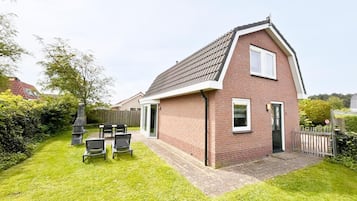 A single-story brick house with a sloped roof, a patio with a table and chairs, and a fenced yard.