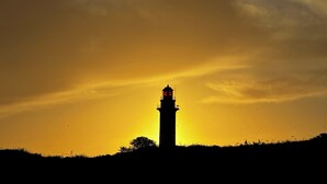 Silhueta de um farol contra um céu de pôr do sol.