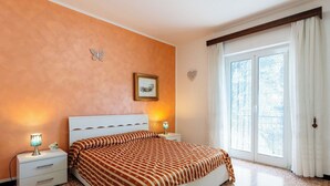 A bedroom with a bed, two bedside tables, a nightstand, a window with curtains, and a wall-mounted picture. - Lovely apartment for 6 people with WIFI and balcony (Riva Ligure)