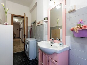 Ein kleines Badezimmer mit Waschmaschine, Waschbecken und Spiegel.