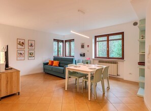 Ein modernes Wohnzimmer mit Essbereich, einer Couch mit Kissen, einem Couchtisch und einem Fernseher auf einer Holzkommode.