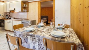 Een eetgedeelte met een tafel voor vier personen, een keuken met houten keukenkastjes, en een bed op de achtergrond.