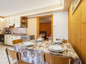 Ein Essbereich mit Tisch für vier Personen, eine Küche mit Holzschränken und ein Bett im Hintergrund.
