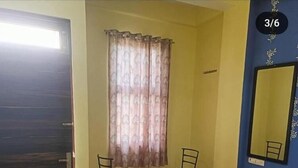 A room with a wooden floor, a bed, two chairs, a window with curtains, and a door. - Shree Siddhivinayak Hotel  (Achrol)