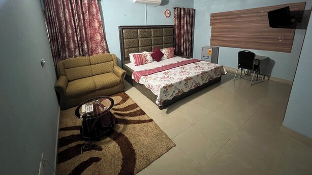 A bedroom with a bed, a sofa, a small table, a ceiling fan, and an air conditioning unit. - Paskandy Hotel (Amasaman)