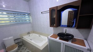 A bathroom with a bathtub, toilet, sink, and a mirror cabinet. - Paskandy Hotel (Amasaman)