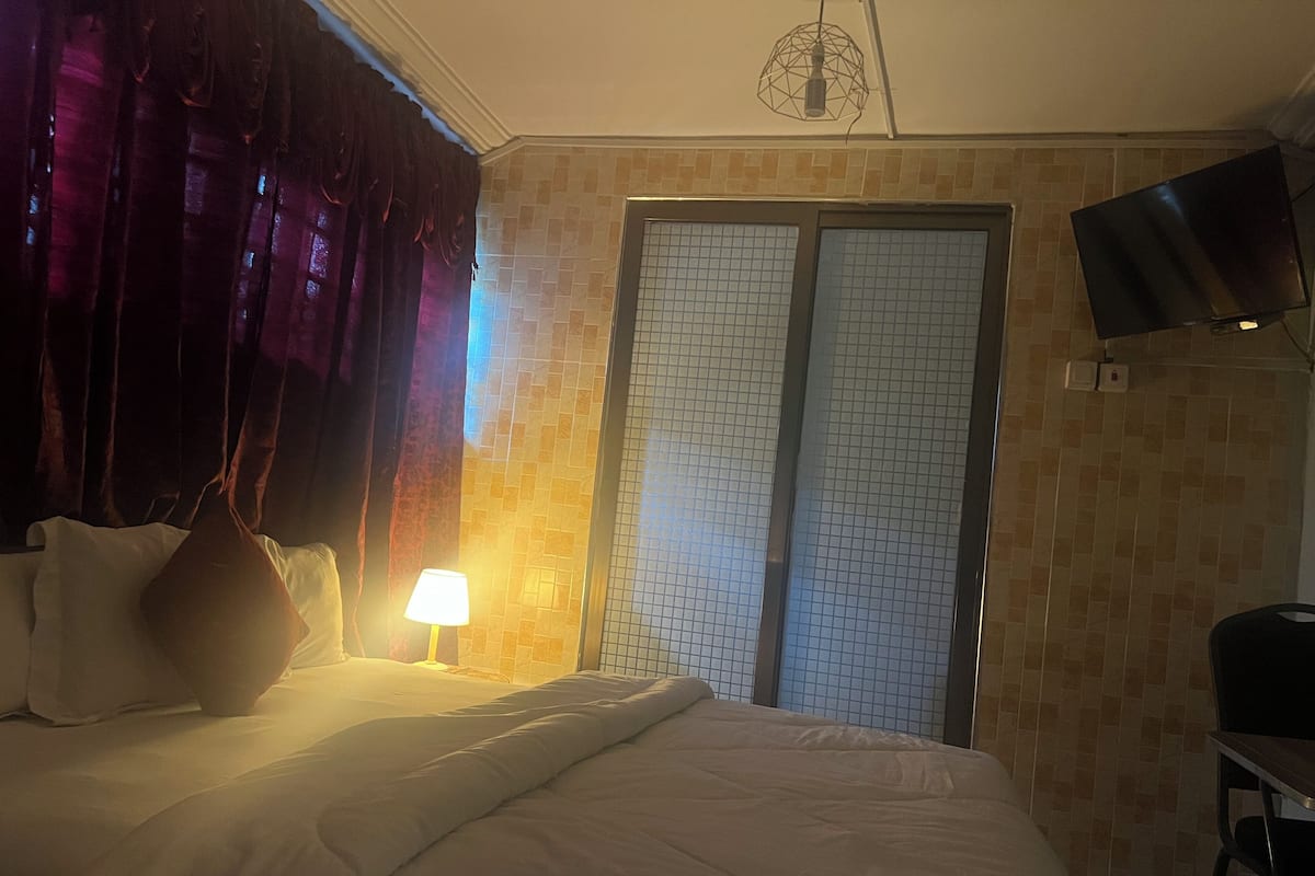 Ein Hotelzimmer mit einem Bett, einer Lampe, einem an der Wand befestigten Fernseher und einer Tür mit einem Gittermuster.