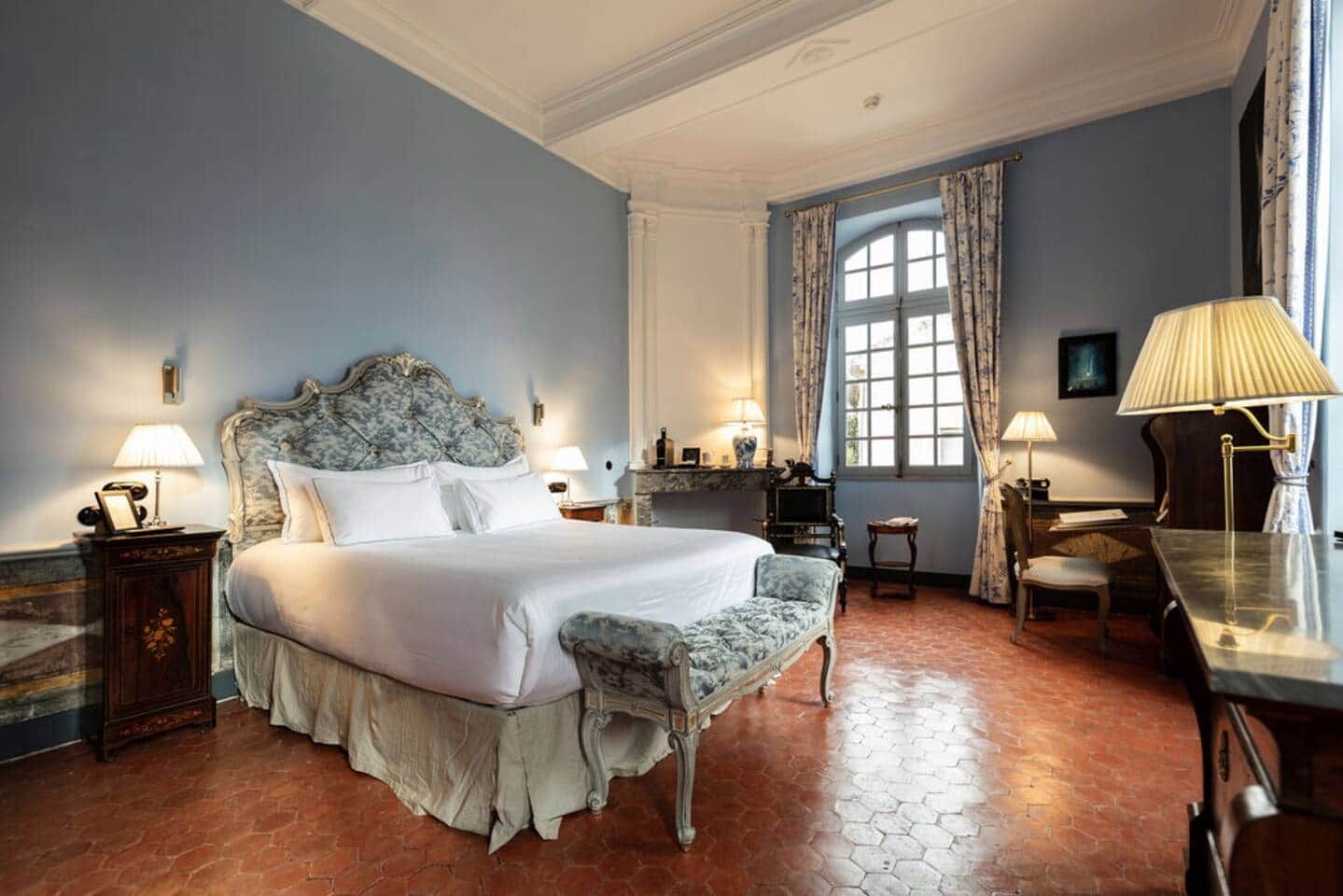 A hotel room with a large bed, a desk, a chair, and a window with curtains.