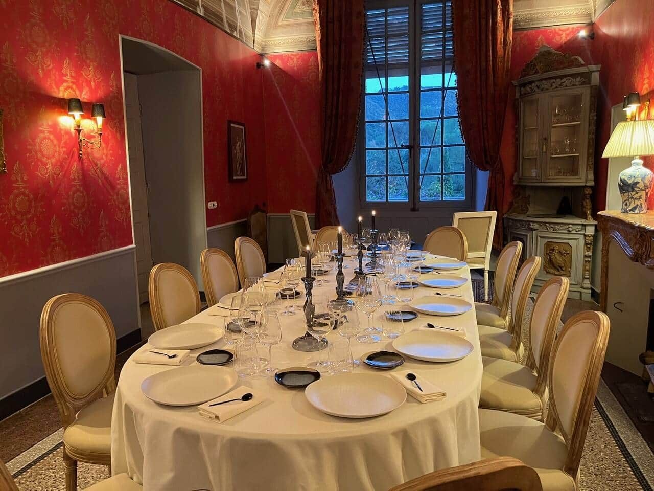 A formal dining room with a long table set for a meal, elegant chairs, and a view through a window.