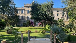 A wooden bridge leading to a large building with a garden in front.