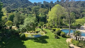 A well-maintained garden with a swimming pool, surrounded by lush greenery and hills in the background.