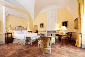 A hotel room with a large bed, a sitting area with a chair and table, a fireplace, and two lamps.