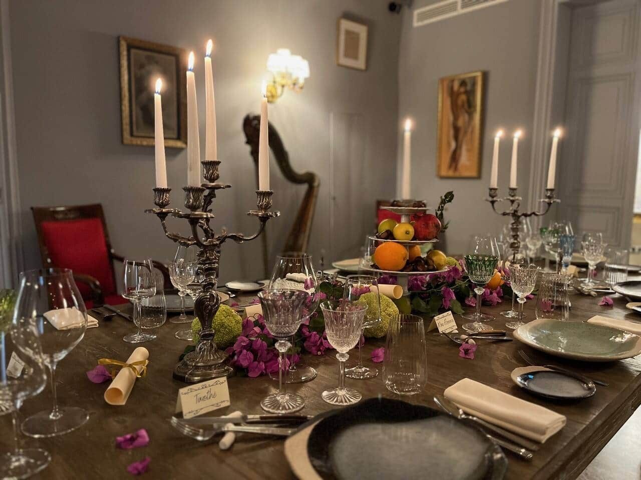 Une table à manger décorée avec de nombreuses bougies, de la verrerie et un centre de table composé de fruits.