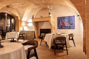 A dining area with tables set for two, a fireplace, and a painting on the wall.