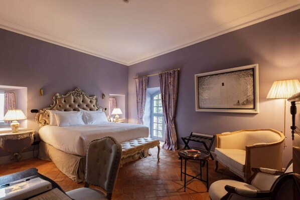 Une chambre d’hôtel avec un grand lit, un coin salon comprenant une chaise et une table, une lampe et un tableau au mur.