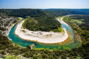 A coastal landscape with a river curving through a forested area, surrounded by hills.