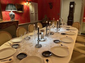 Une table à manger élégante, dressée avec des bougies, des verres et des assiettes, dans une pièce aux murs rouges et ornée d’une horloge.