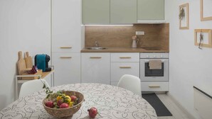 Una cucina compatta con pensili bianchi, un piano di lavoro in legno, un lavello e un fornello. È presente un tavolo da pranzo con un cesto di frutta e una macchina da caffè.