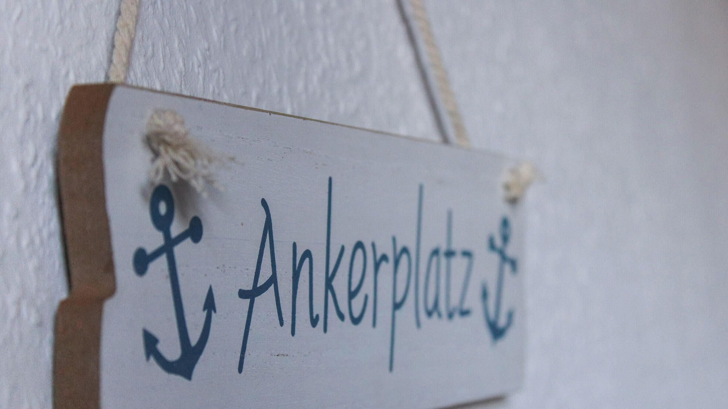 A wooden sign with an anchor symbol and the text "Ankerplatz" hanging on a wall.