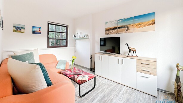 Uma sala de estar moderna com um sofá, uma mesa de centro, uma TV e um armário. Há uma janela com vista para o exterior.