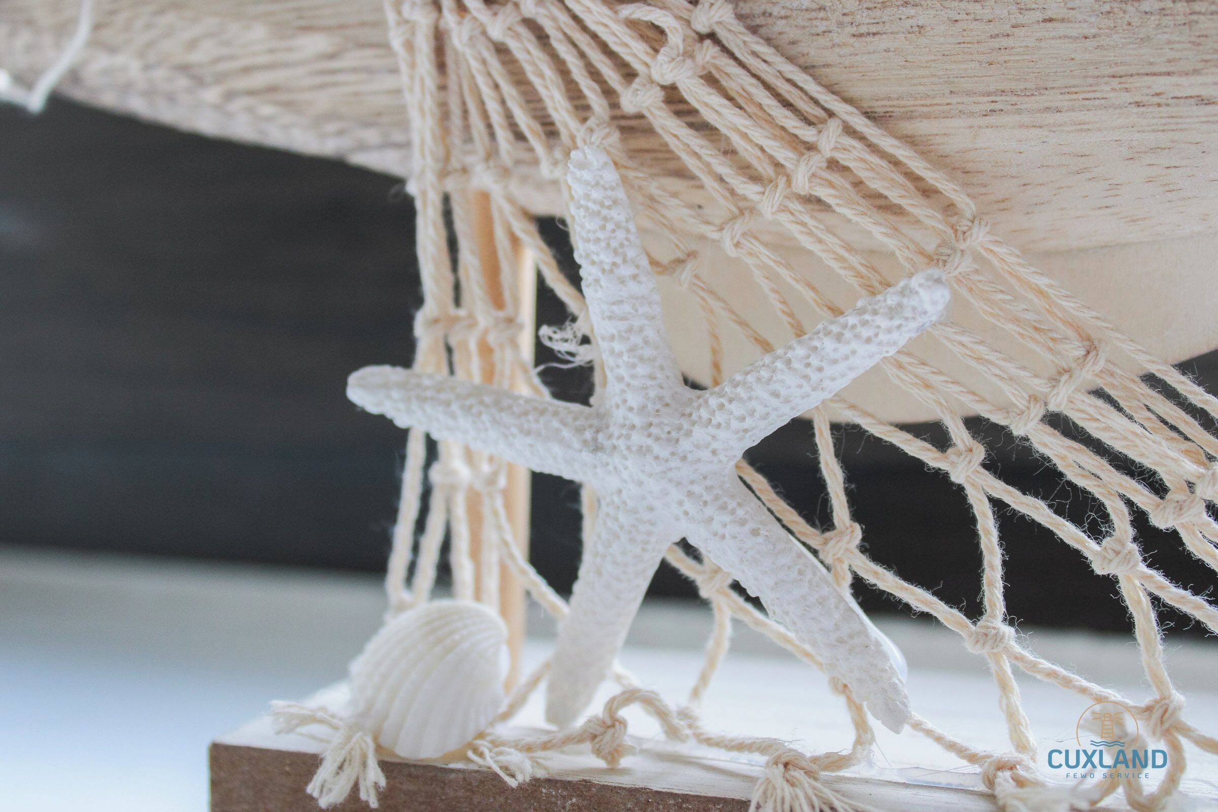 Un adorno de macramé con una estrella de mar y una concha marina sobre un bloque de madera.