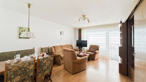 Uma sala de estar com um sofá, televisão e mesa de jantar com cadeiras.