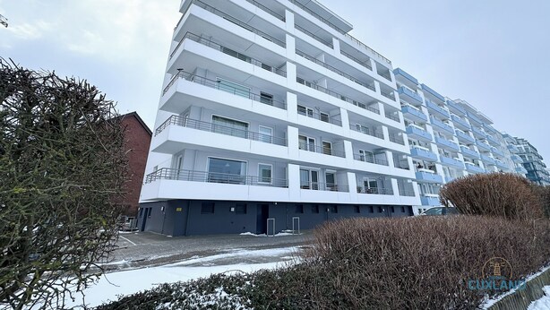 Edifício residencial com várias andares, varandas, área de estacionamento e terreno coberto de neve.