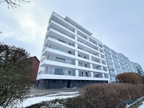Een meerlaags woongebouw met balkons, een parkeerplaats en een met sneeuw bedekte grond.