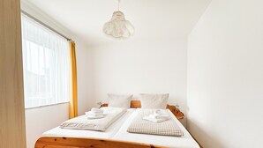 Uma cama de casal bem arrumada, com roupa de cama xadrez, uma cabeceira de madeira e uma mesinha de cabeceira com abajur.