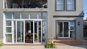 A two-story house with a patio, large sliding glass doors, and a balcony with outdoor furniture. - me-Elohim  (Mossel Bay)
