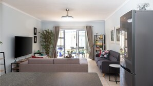 A living room with a flat-screen TV, sofa, dining table, chairs, and a refrigerator. - me-Elohim  (Mossel Bay)
