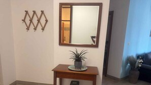 A wooden console table with a potted plant, a mirror, and a trash bin in a room with tiled flooring and a blue wall. - Holiday apartment with air conditioning and balcony (Poreč)