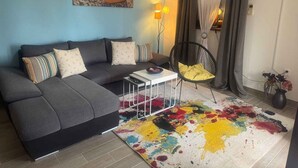 A living room with a grey sofa, a colorful rug, a black chair, and a painting on the wall. - Holiday apartment with air conditioning and balcony (Poreč)
