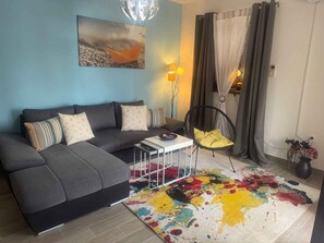 Uma sala de estar com um sofá cinza, um tapete colorido, uma cadeira preta e uma pintura na parede.