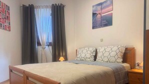 A bedroom with a bed, a nightstand, a lamp, a window with curtains, and a wall art piece. - Holiday apartment with air conditioning and balcony (Poreč)